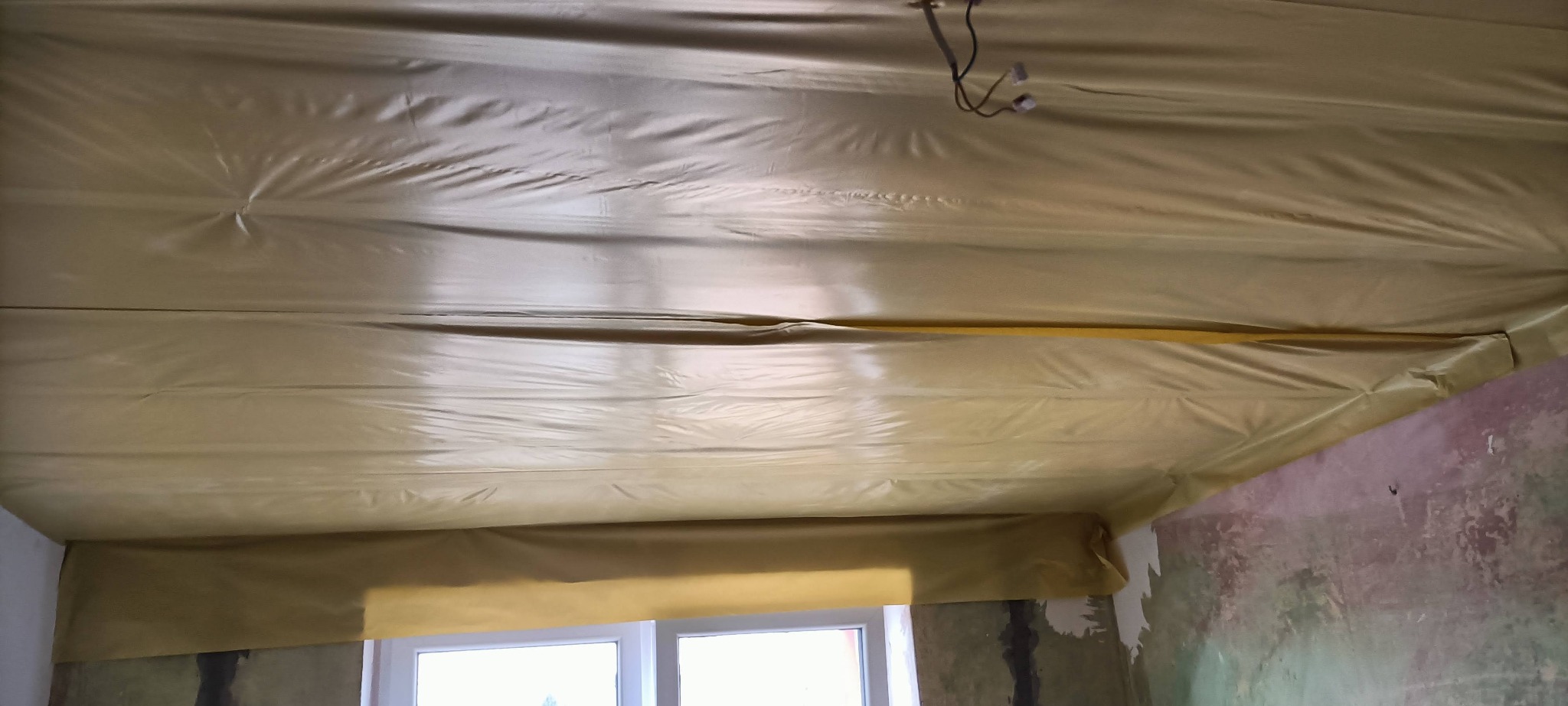 Przygotowanie do remontu: Sufit i ściany zabezpieczone folią ochronną przed zabrudzeniem, widoczne wiszące przewody elektryczne. Okno w dolnej części kadru.