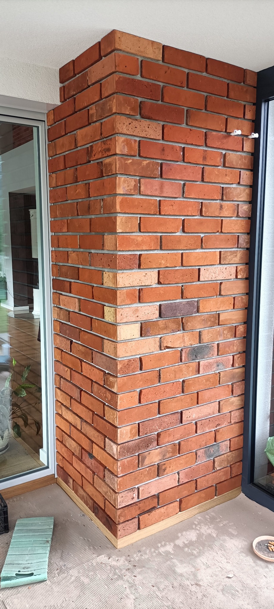 Wykończony narożnik ścian z cegły klinkierowej wewnątrz budynku, widoczny fragment okna i podłogi. Jasne spoiny podkreślają regularny układ cegieł.