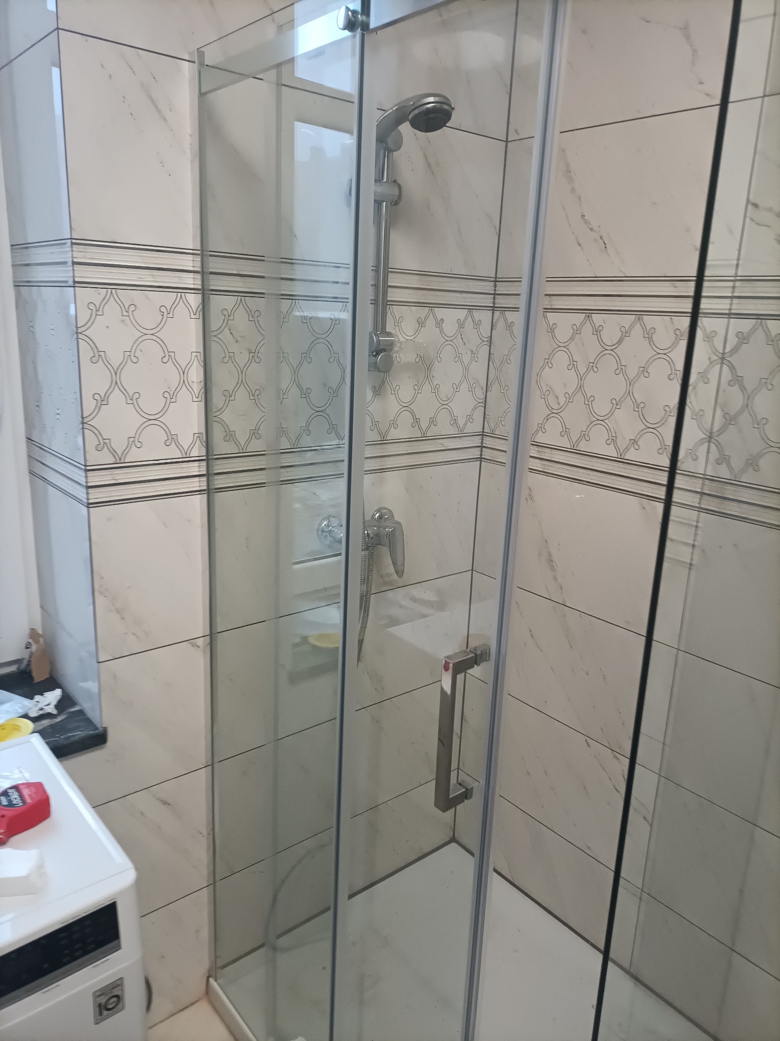 Wykończona kabina prysznicowa z chromowaną armaturą, zamontowana w łazience z białymi płytkami imitującymi marmur i dekoracyjnym wzorem.