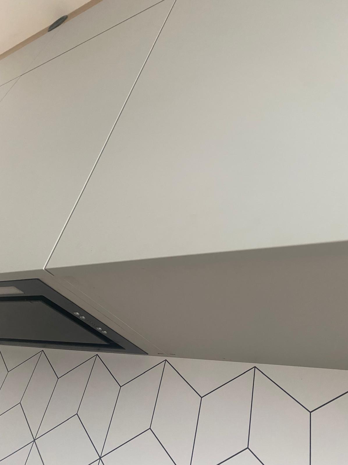 Białe szafki kuchenne z okapem i geometrycznymi płytkami na ścianie. Ujęcie z dołu, podkreślające nowoczesny design kuchni.