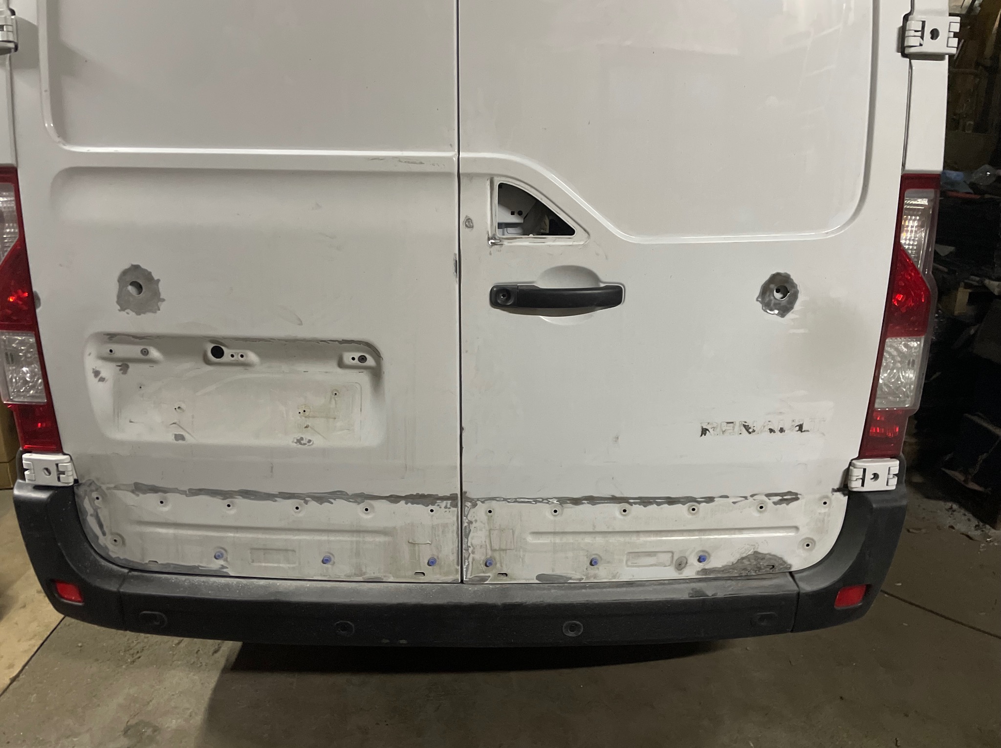 Biały van z uszkodzeniami karoserii w trakcie naprawy: widoczne dziury, szpachla i brakujące elementy. Prace blacharskie i przygotowanie do lakierowania.