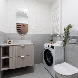 RENOPLAN Projekty i Wykończenia Wnętrz - Nowoczesna łazienka w Szczecinie z szarą glazurą, wiszącą szafką z umywalką i pralką. Lustro owalne z podświetleniem, minimalistyczny grzejnik drabinkowy.