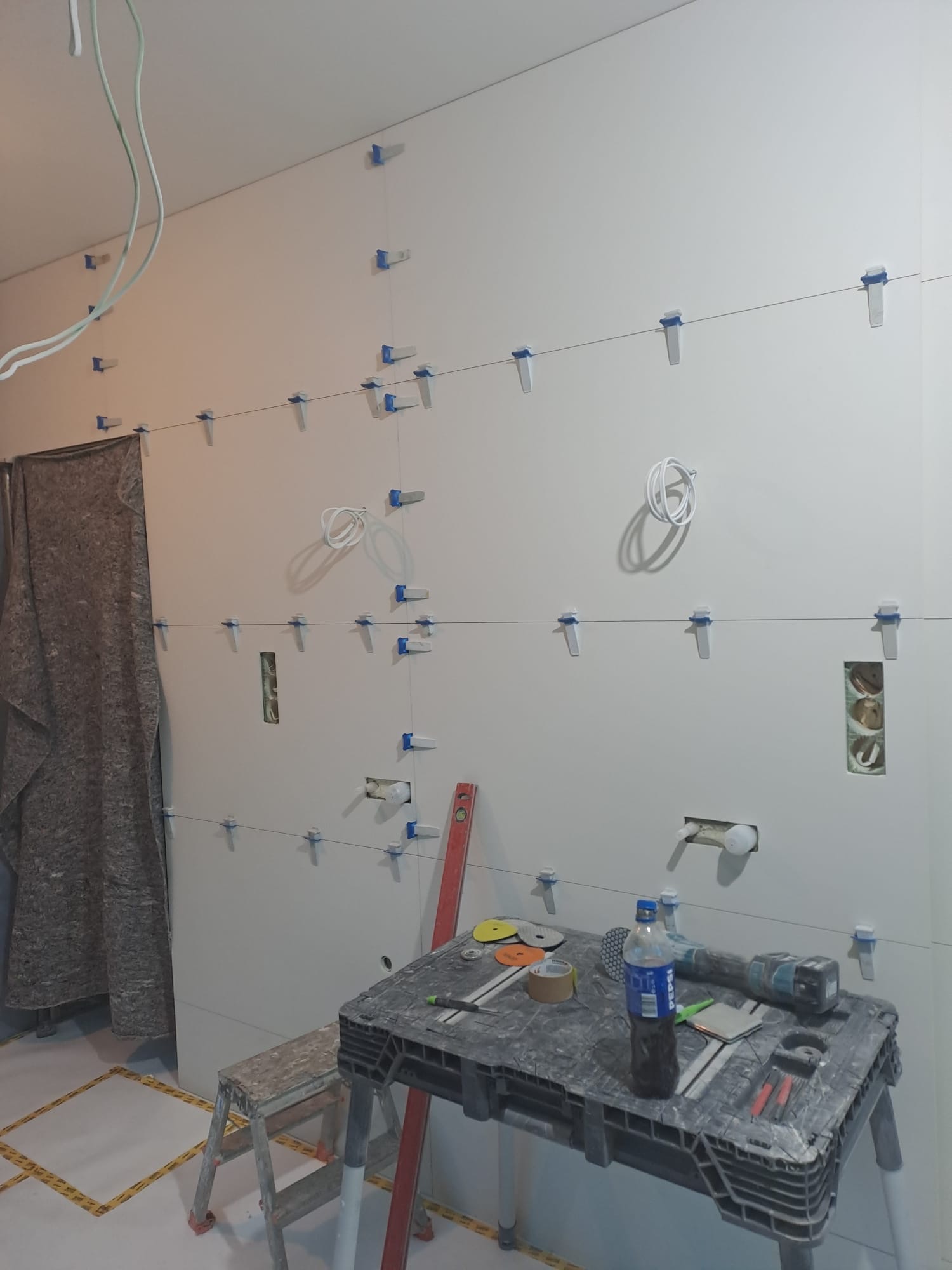 Ściana z płyt kartonowo-gipsowych w trakcie montażu, z widocznymi elementami mocującymi, poziomica i narzędzia na stole roboczym. Przygotowanie do wykończenia wnętrz.