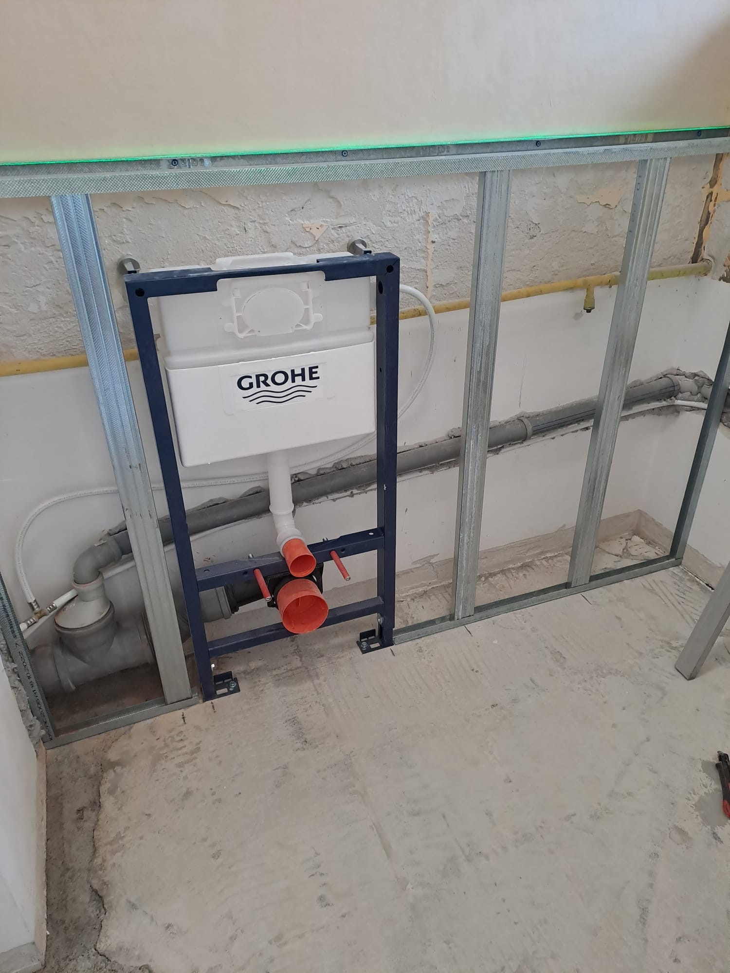 Stelaż podtynkowy Grohe zamontowany w łazience, widoczne rury i profile metalowe, przygotowanie do montażu WC, poziomica laserowa na górze.