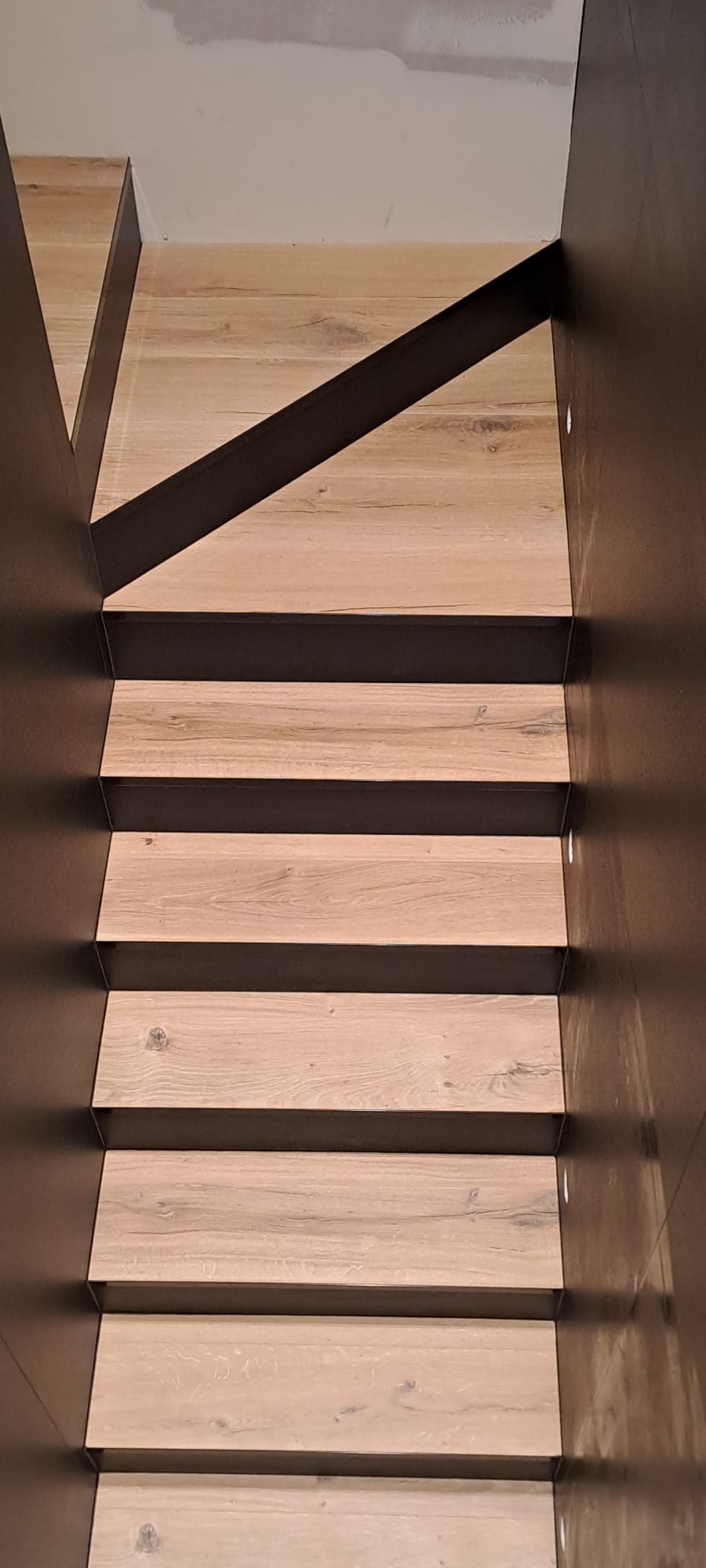 Nowoczesne schody z drewnianymi stopniami i ciemnymi, metalowymi elementami konstrukcyjnymi. Widok z góry, oświetlenie punktowe.