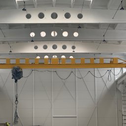 Pw Bartosz Olszewski - Wnętrze hali po malowaniu: białe ściany z panelami, żółty suwnicowy dźwig i oświetlenie. Widoczna drabina i elementy konstrukcyjne.