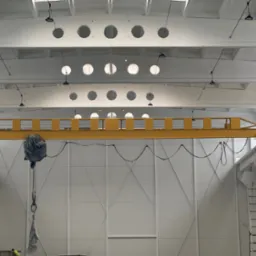 Wnętrze hali po malowaniu: białe ściany z panelami, żółty suwnicowy dźwig i oświetlenie. Widoczna drabina i elementy konstrukcyjne.