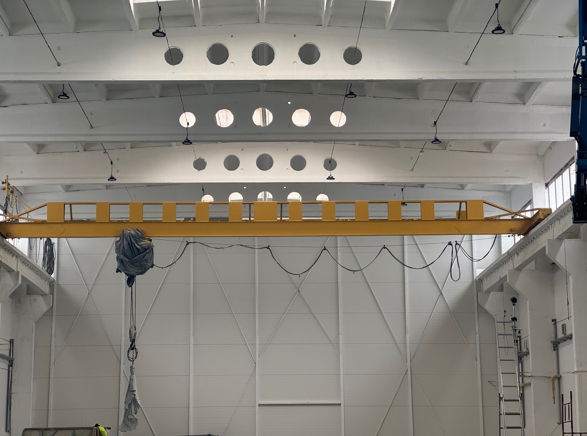 Wnętrze hali po malowaniu: białe ściany z panelami, żółty suwnicowy dźwig i oświetlenie. Widoczna drabina i elementy konstrukcyjne.