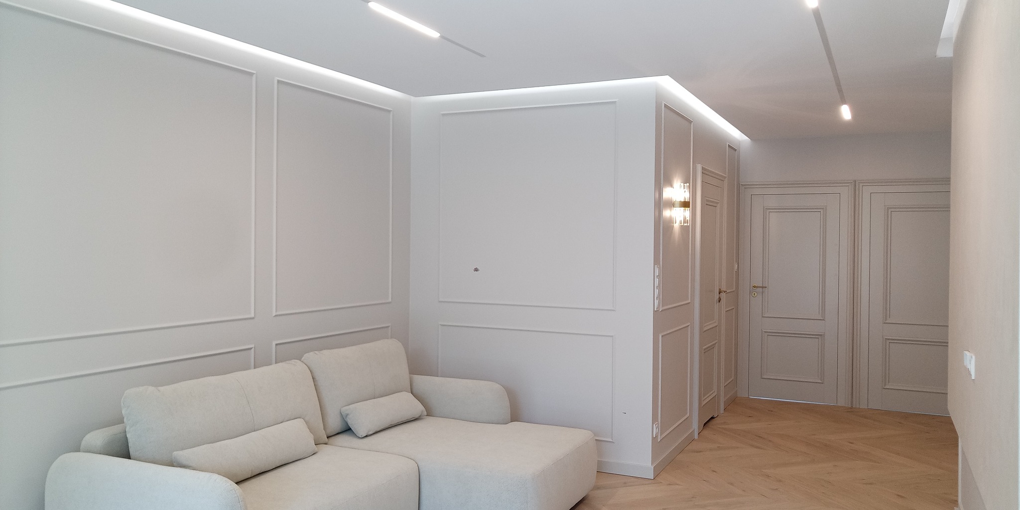 Eleganckie wykończenie wnętrza: kremowy narożnik, ściany z dekoracyjnymi listwami, parkiet w jodełkę i oświetlenie LED. Dwoje drzwi z ozdobnymi płycinami.