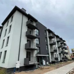 Nowoczesny, dwukolorowy blok z balkonami, widok z dołu, ukazujący elewację po remoncie, z elementami wykończeniowymi i kostką brukową w otoczeniu.