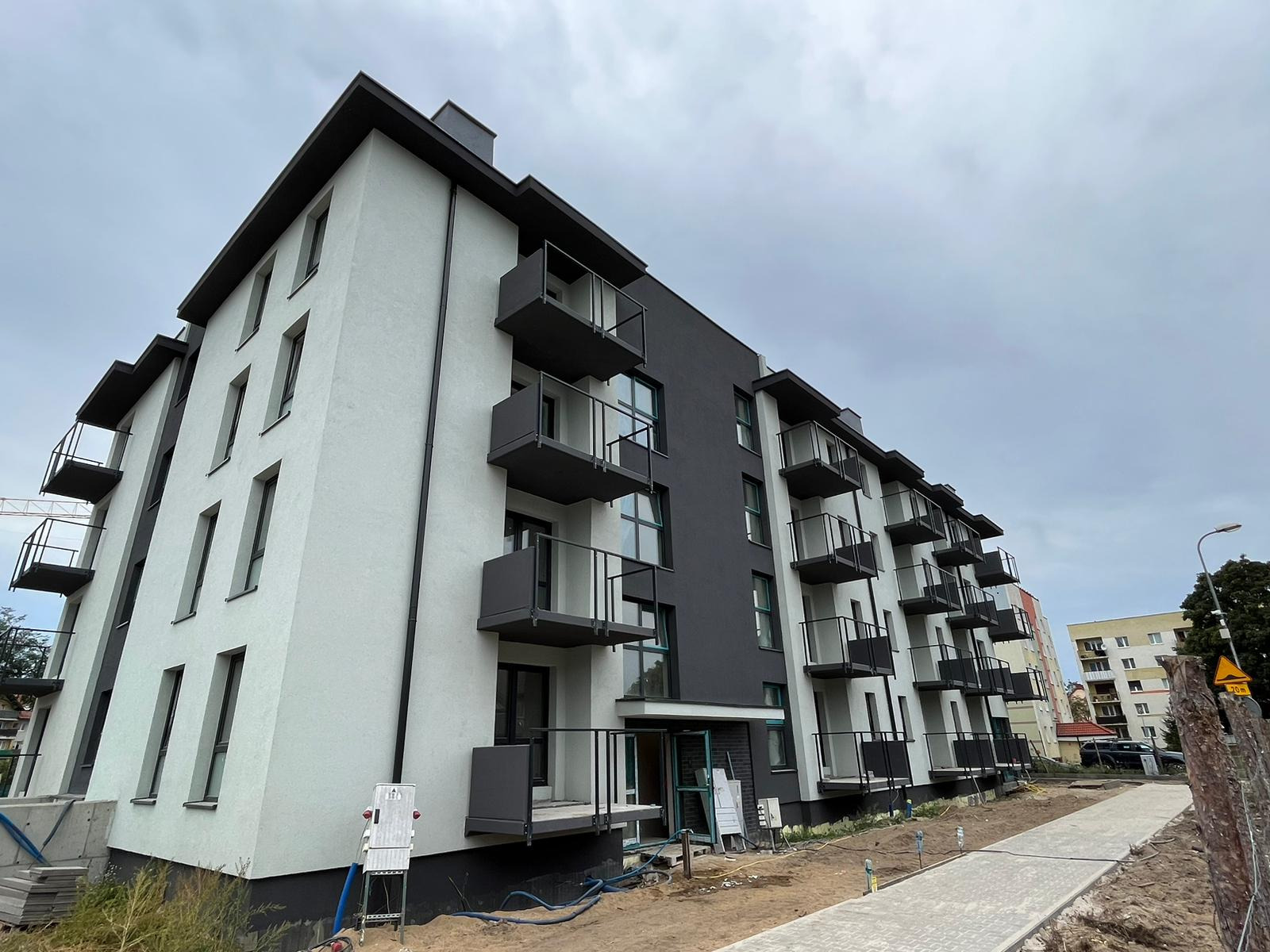 Nowoczesny, dwukolorowy blok z balkonami, widok z dołu, ukazujący elewację po remoncie, z elementami wykończeniowymi i kostką brukową w otoczeniu.