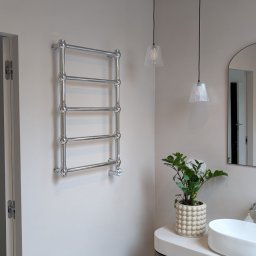 Studio Mikrocement - Nowoczesna łazienka z grzejnikiem drabinkowym, umywalką nablatową i podłogą w odcieniach beżu. Dwie lampy wiszące i roślina doniczkowa dodają przytulności.