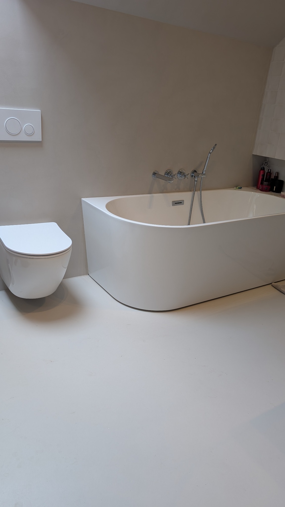 Biała, nowoczesna łazienka z podłogą i ścianami w jasnym odcieniu beżu. Widoczna wanna, toaleta podwieszana i armatura. Minimalistyczny design.