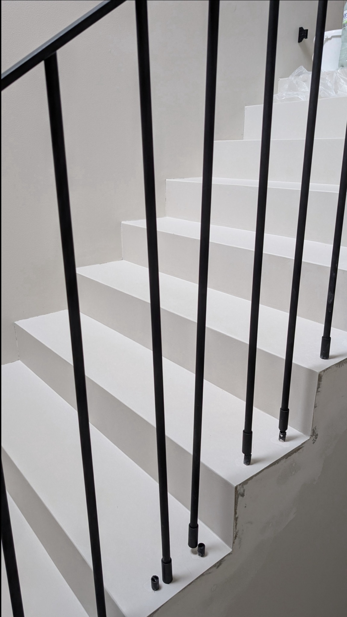 Schody wykończone w jasnym odcieniu z czarną, minimalistyczną balustradą. Widoczne niedoskonałości przy montażu poręczy.