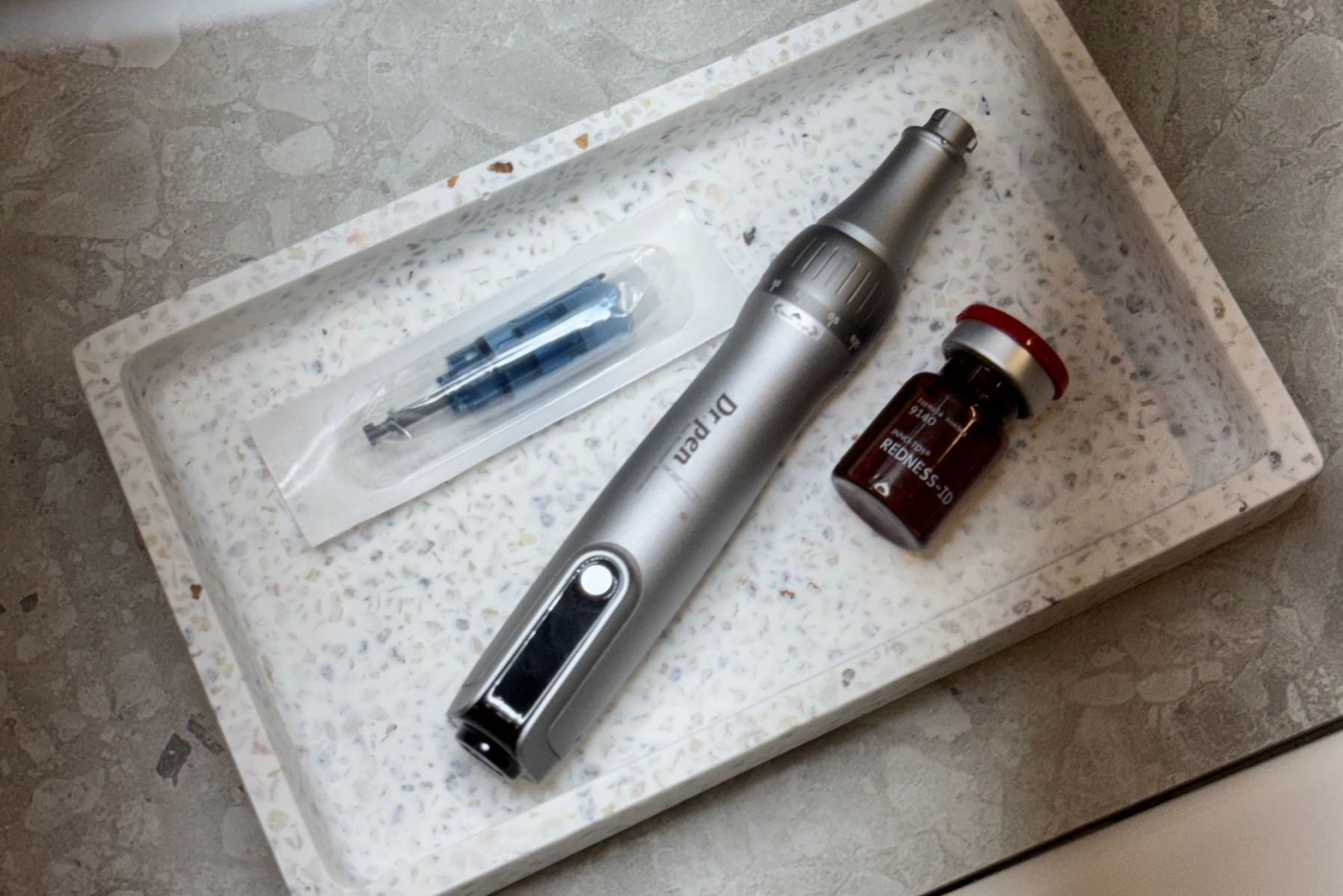 Zestaw do mezoterapii mikroigłowej: Dr. Pen, sterylna igła w opakowaniu i ampułka Redness-TD na wzorzystej tacy, gotowy do zabiegu w gabinecie kosmetycznym.