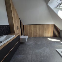 Inspiro-Meble Przemysław Wierzbicki - Nowoczesna łazienka na poddaszu z drewnianą szafą w zabudowie, czarną umywalką i szarą podłogą. Okno dachowe wpuszcza jasne światło.