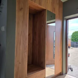 Funkcjonalna szafa wnękowa z lustrem i wieszakami, wykończona w ciepłym odcieniu drewna, idealna do przedpokoju. Widok z perspektywy wejścia do domu.