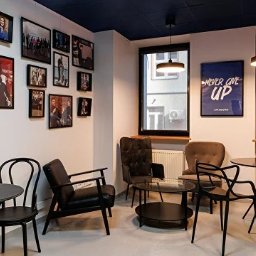 QS BUD - Nowoczesne wnętrze kawiarni z ciemnym sufitem, czarnymi meblami i galerią zdjęć na ścianie, oświetlone lampami wiszącymi. Widok na zewnątrz przez okna.
