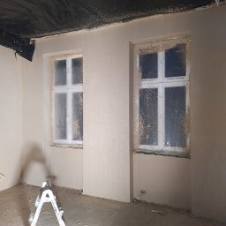PROBUD ST SPÓŁKA Z OGRANICZONĄ ODPOWIEDZIALNOŚCIĄ - Pokój po nałożeniu gładzi, widoczne dwa okna zabezpieczone folią, drabina malarska i listwy przypodłogowe na podłodze. Sufit zabezpieczony folią malarską.