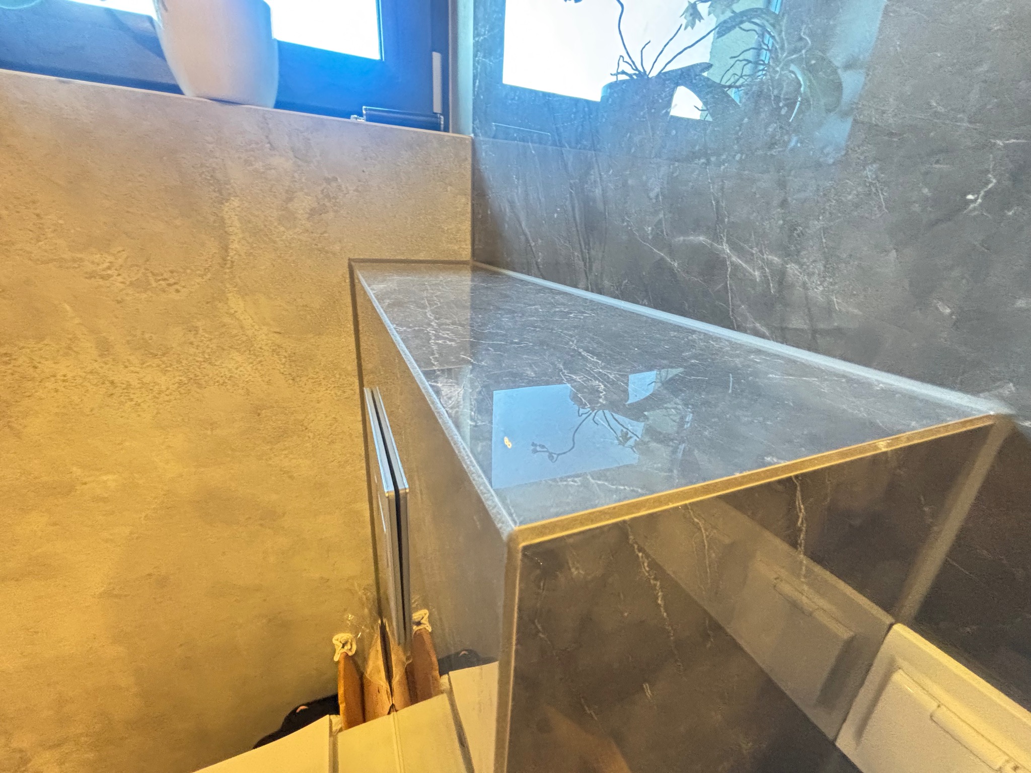 Wykończona łazienka z blatem z szarego marmuru, widoczne narzędzia malarskie. Ściany wykończone w odcieniach beżu i szarości. Nowoczesny design.