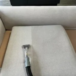 Pranie jasnej tapicerki sofy specjalistycznym odkurzaczem. Widoczna różnica w czystości po lewej stronie, ciemne meble w tle. Efekt czyszczenia na siedzisku.