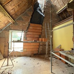 PT-BUD Piotr Tęcza - Poddasze w trakcie przebudowy: widoczne cegły, rusztowania, izolacja dachu i okno. Częściowo wykończona ściana z cegły ceramicznej.