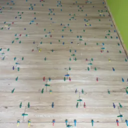 Układanie podłogi z płytek imitujących drewno, z użyciem kolorowych klipsów poziomujących. Widoczne fragmenty ścian w odcieniach beżu i zieleni.