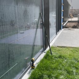 PT-BUD Piotr Tęcza - Montaż okien przesuwnych w nowoczesnym domu. Widoczny profil okienny, narzędzia i trawnik. Okna odbijają otoczenie, tworząc ciekawy efekt wizualny.