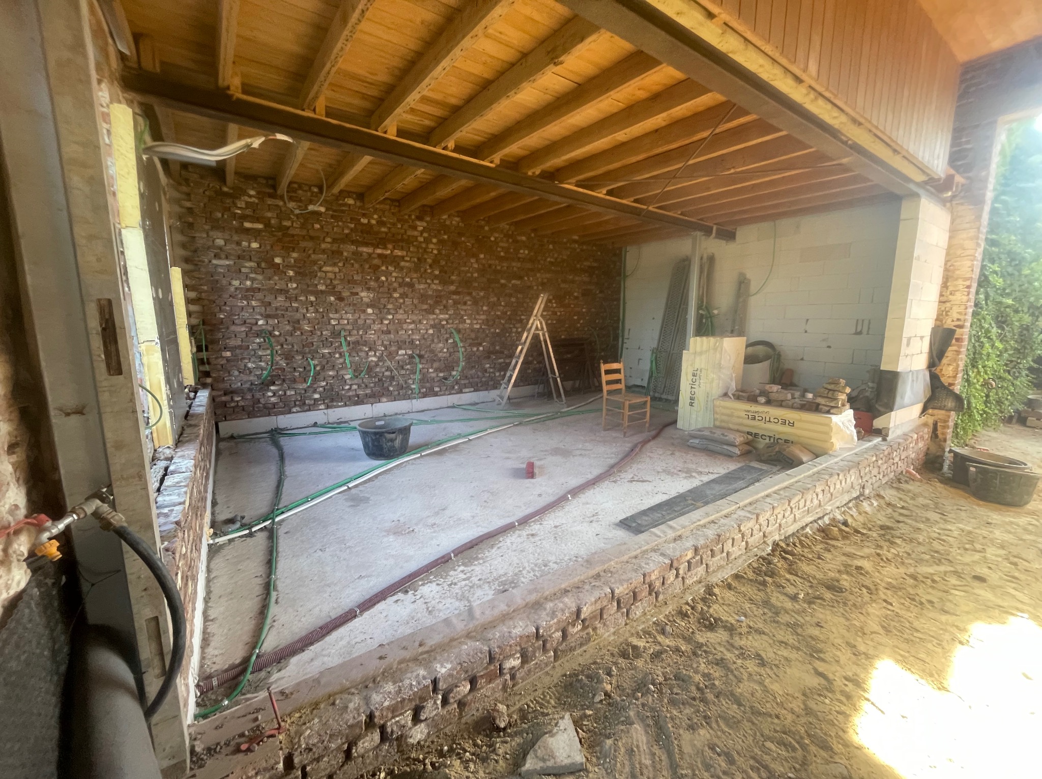 Remont balkonu: widok na wnętrze z ceglaną ścianą, instalacją, drewnianym stropem i materiałami budowlanymi. Etap prac przed wykończeniem.