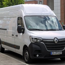 In time - Renault Master w miejskiej scenerii, z widocznym numerem rejestracyjnym i odbiciem chmur na szybie, zaparkowany przy chodniku z zielenią w tle.