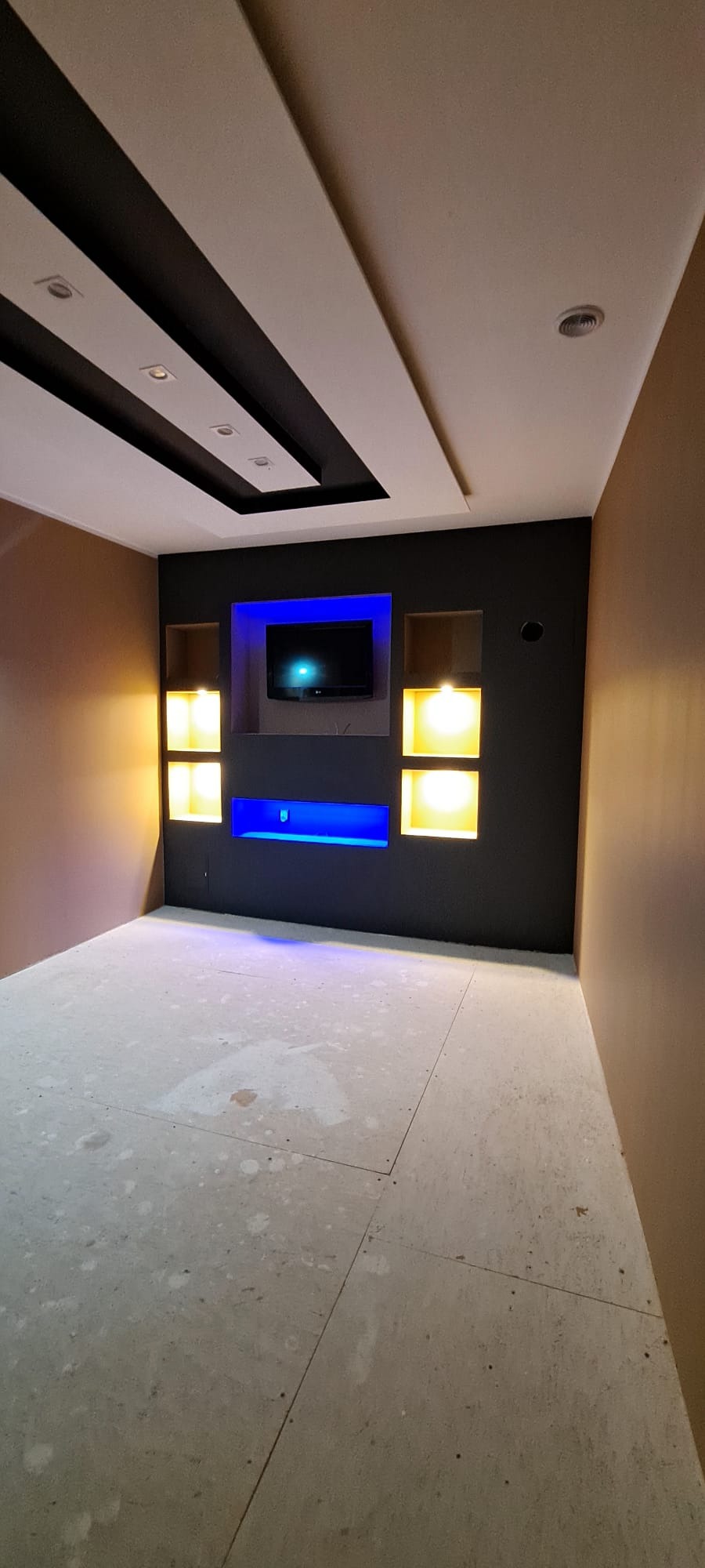 Nowoczesne wykończenie wnętrza z podwieszanym sufitem, oświetleniem LED w kolorze niebieskim i żółtym oraz ścianą w odcieniach brązu i czerni. Podłoga w stanie surowym.