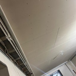 FReshHome Robert Famuła - Sufit z płyt karton-gips z widoczną konstrukcją metalową i instalacją elektryczną, przygotowany do dalszych prac wykończeniowych. Widok z dołu, surowy stan.