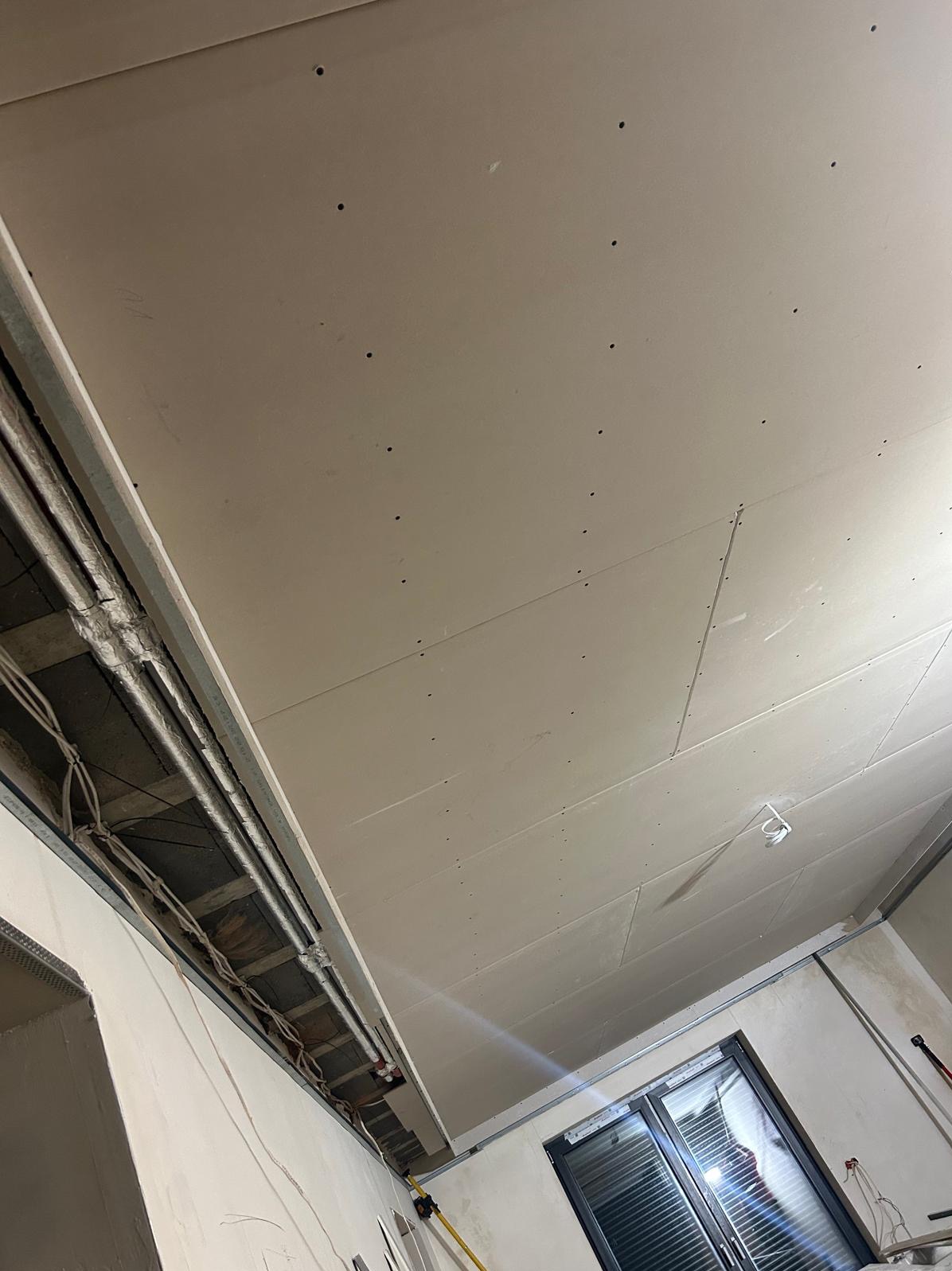 Sufit z płyt karton-gips z widoczną konstrukcją metalową i instalacją elektryczną, przygotowany do dalszych prac wykończeniowych. Widok z dołu, surowy stan.