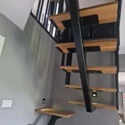 Nowoczesne schody drewniane z metalową konstrukcją, zamontowane przy szarej ścianie z wbudowanym oświetleniem. Minimalistyczny design.