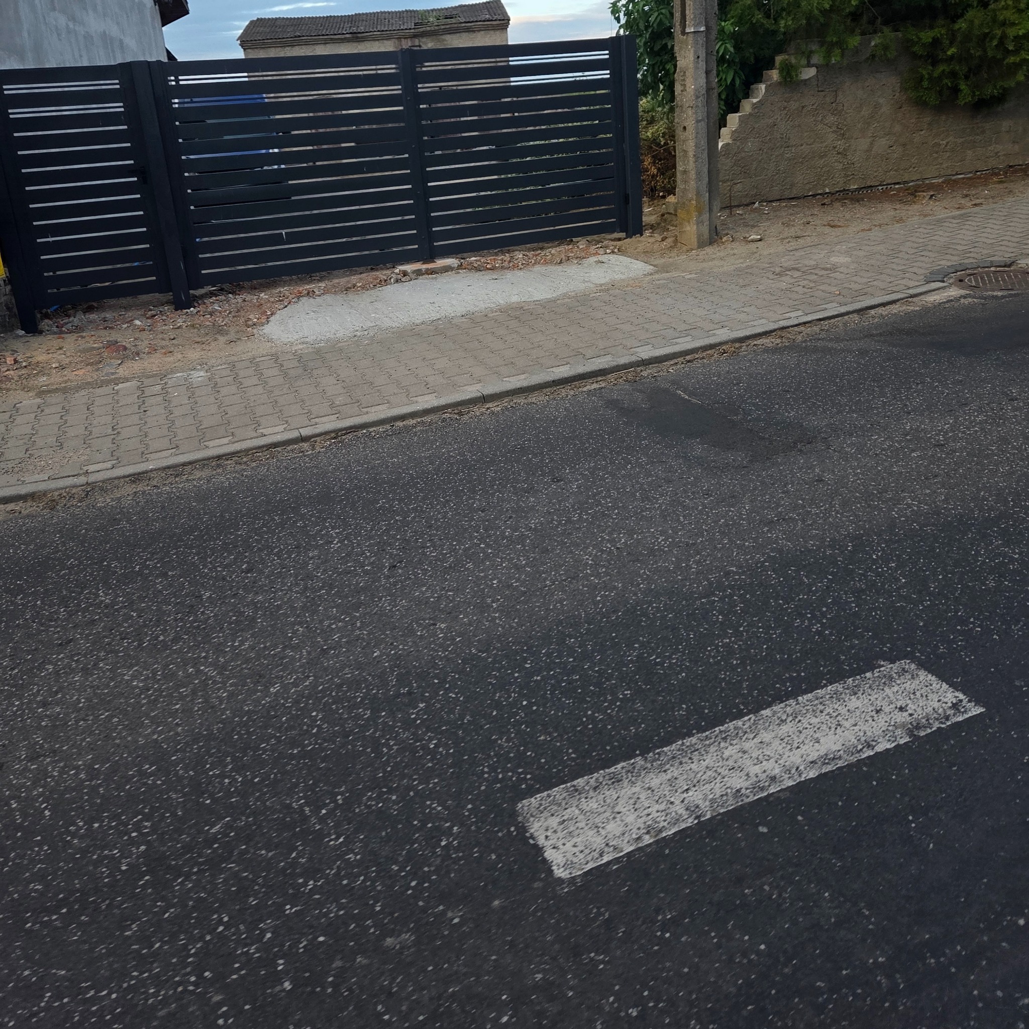 Nowoczesna, pozioma, metalowa brama wjazdowa w kolorze grafitowym. Widok z ulicy, z fragmentem chodnika i elewacji budynku w tle. Minimalistyczny design.