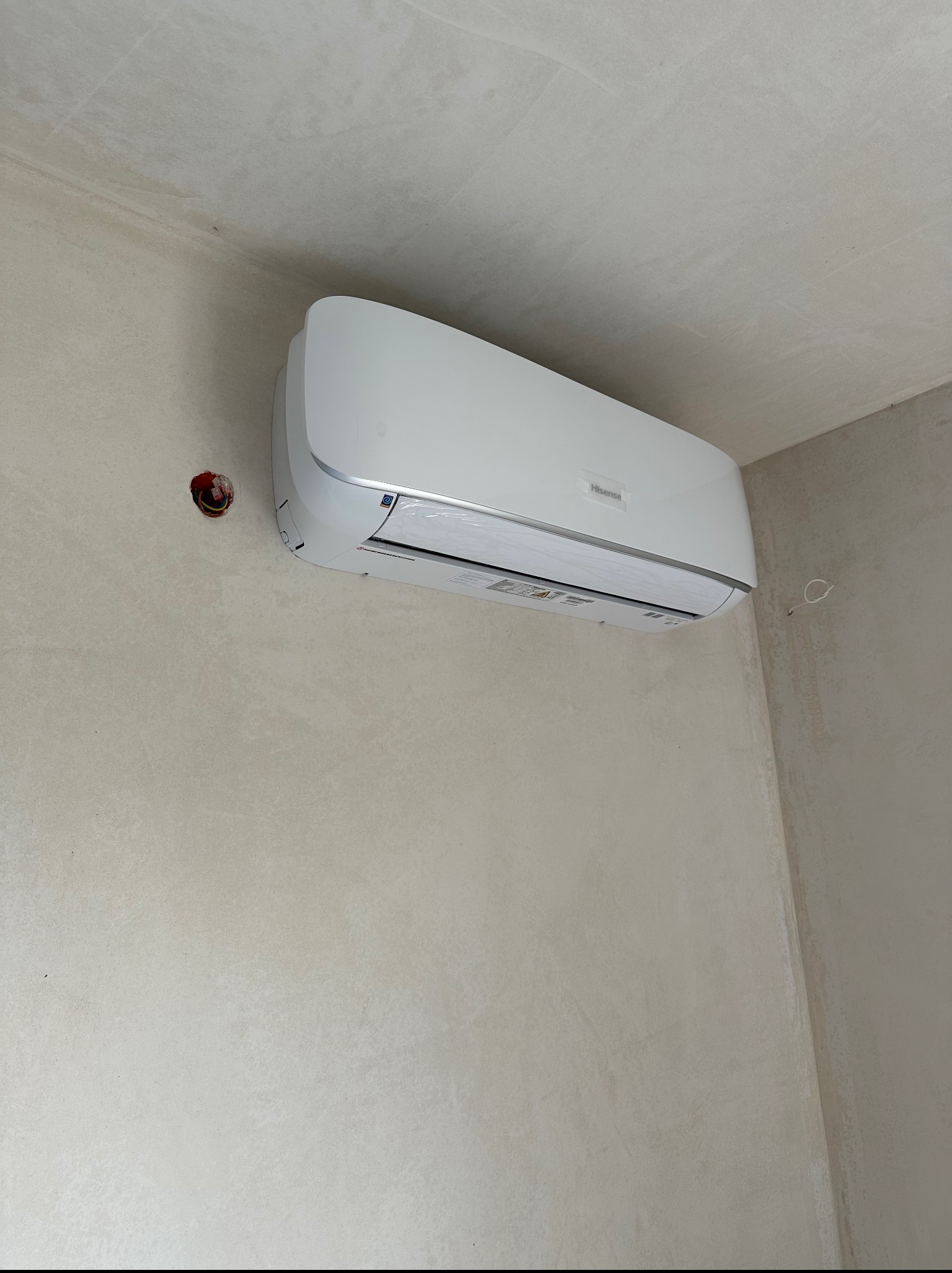 Biały klimatyzator Hisense zamontowany na ścianie w jasnym pomieszczeniu. Widoczne ślady po instalacji elektrycznej.