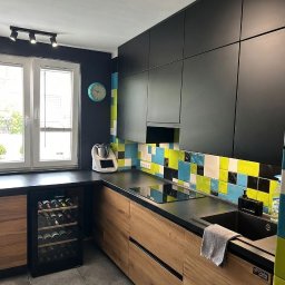 Kussa Meble - Kuchnia w kształcie litery L z czarnymi szafkami górnymi, drewnianymi dolnymi i mozaikowym backsplash'em z płytek w odcieniach niebieskiego, żółtego i czarnego. Zintegrowana płyta indukcyjna...