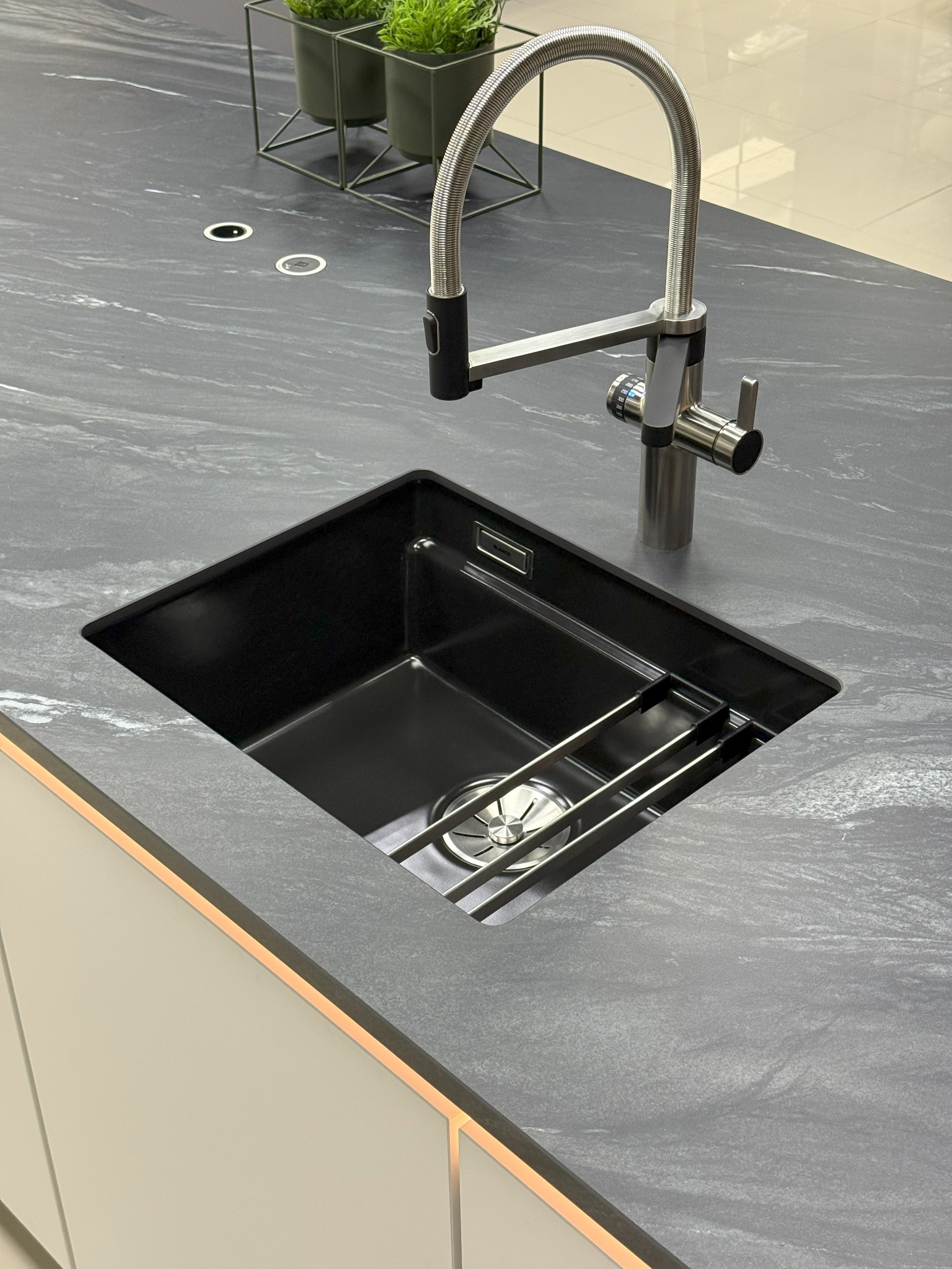 Nowoczesny, czarny zlewozmywak podwieszany w blacie ze spieku kwarcowego, bateria z filtrem wody. Minimalistyczny design i funkcjonalność w kuchni.