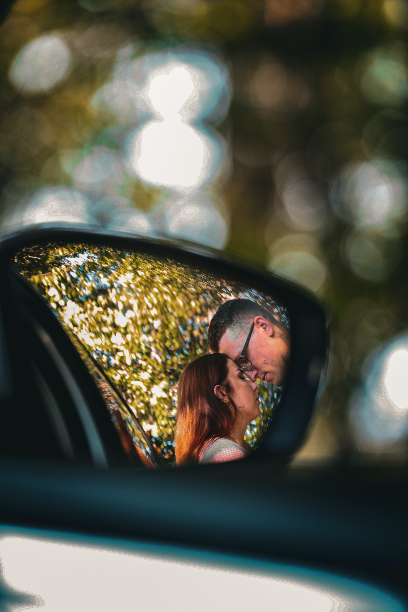 Para całująca się, widziana w lusterku samochodowym na tle zieleni. Unikalne ujęcie z bliska, podkreślające intymność i emocje chwili.