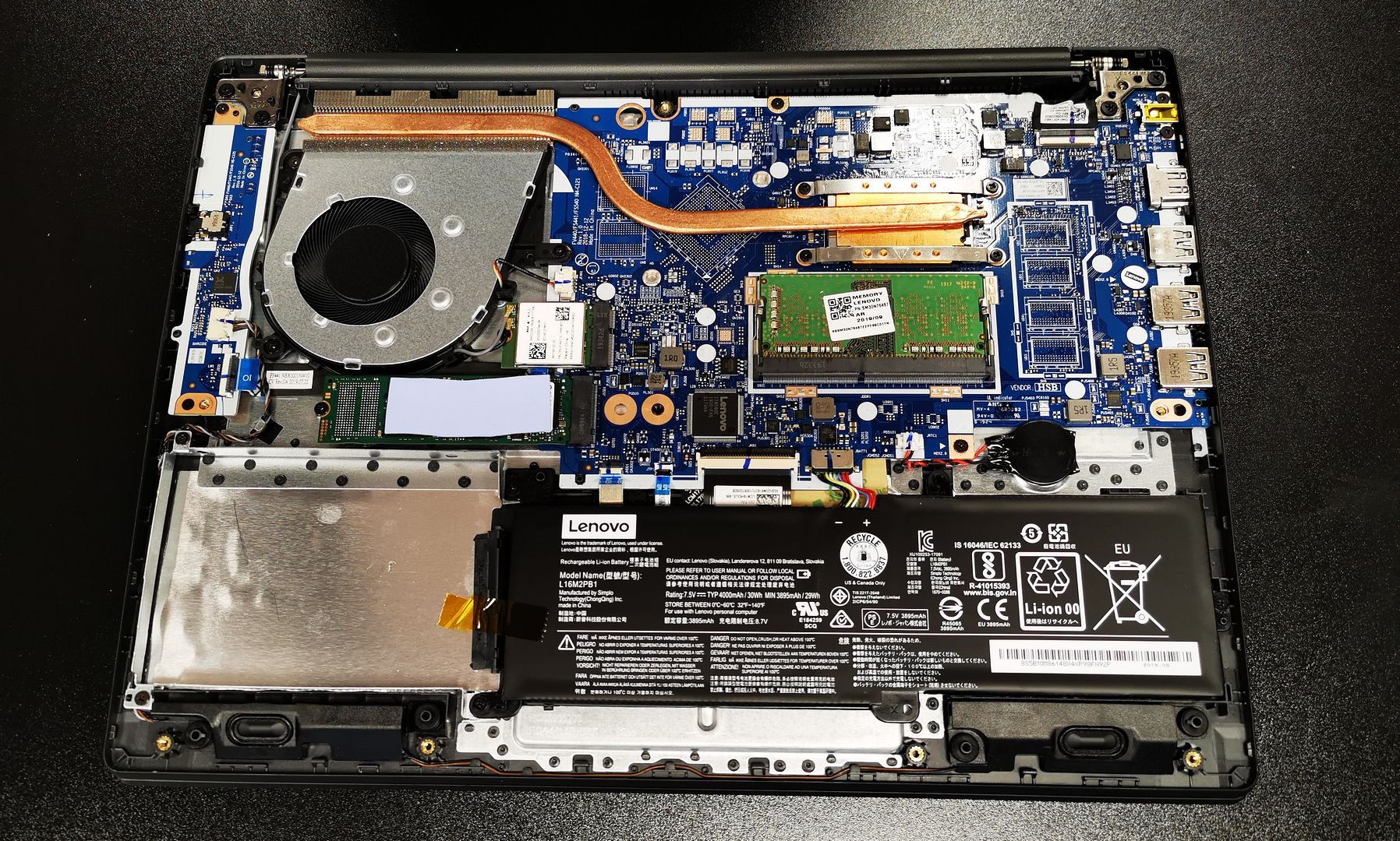 Wnętrze otwartego laptopa Lenovo z widoczną płytą główną, baterią, wentylatorem i elementami chłodzenia. Detaliczny widok na podzespoły komputera.