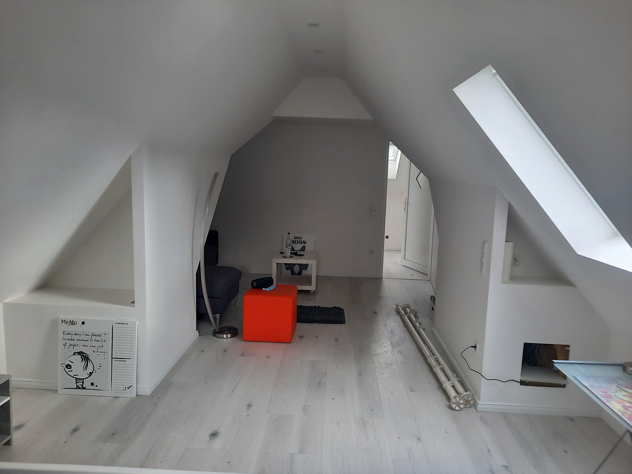 Jasne poddasze po remoncie: białe ściany, podłoga z paneli, okno dachowe. Widoczne meble, lampa i dekoracje. Minimalistyczny styl wykończenia wnętrza.