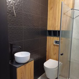 Interior Wykończenia Wnętrz Łukasz Chudzik - Nowoczesna łazienka z czarnymi, trójwymiarowymi płytkami, drewnianymi szafkami i białą ceramiką. Uwagę zwraca minimalistyczna umywalka nablatowa i kabina prysznicowa typu walk-in.