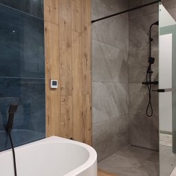 Interior Wykończenia Wnętrz Łukasz Chudzik - Nowoczesna łazienka z kabiną prysznicową typu walk-in, wanną i panelami ściennymi imitującymi drewno. Minimalistyczny design z czarnymi akcentami.