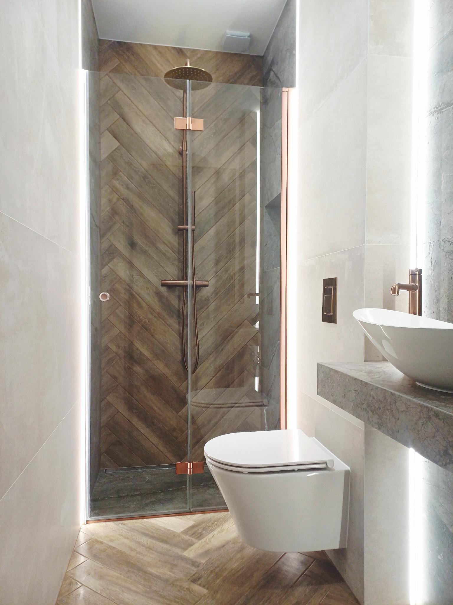 Nowoczesna łazienka z kabiną prysznicową typu walk-in, drewnopodobną glazurą ułożoną w jodełkę, podświetleniem LED i wiszącą miską WC.