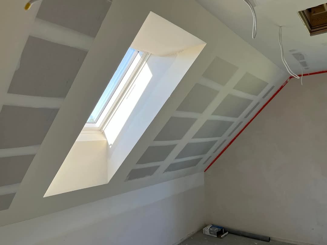 Poddasze z oknem dachowym po montażu płyt kartonowo-gipsowych, widoczne łączenia płyt przygotowane do szpachlowania. Czerwona taśma zabezpieczająca.
