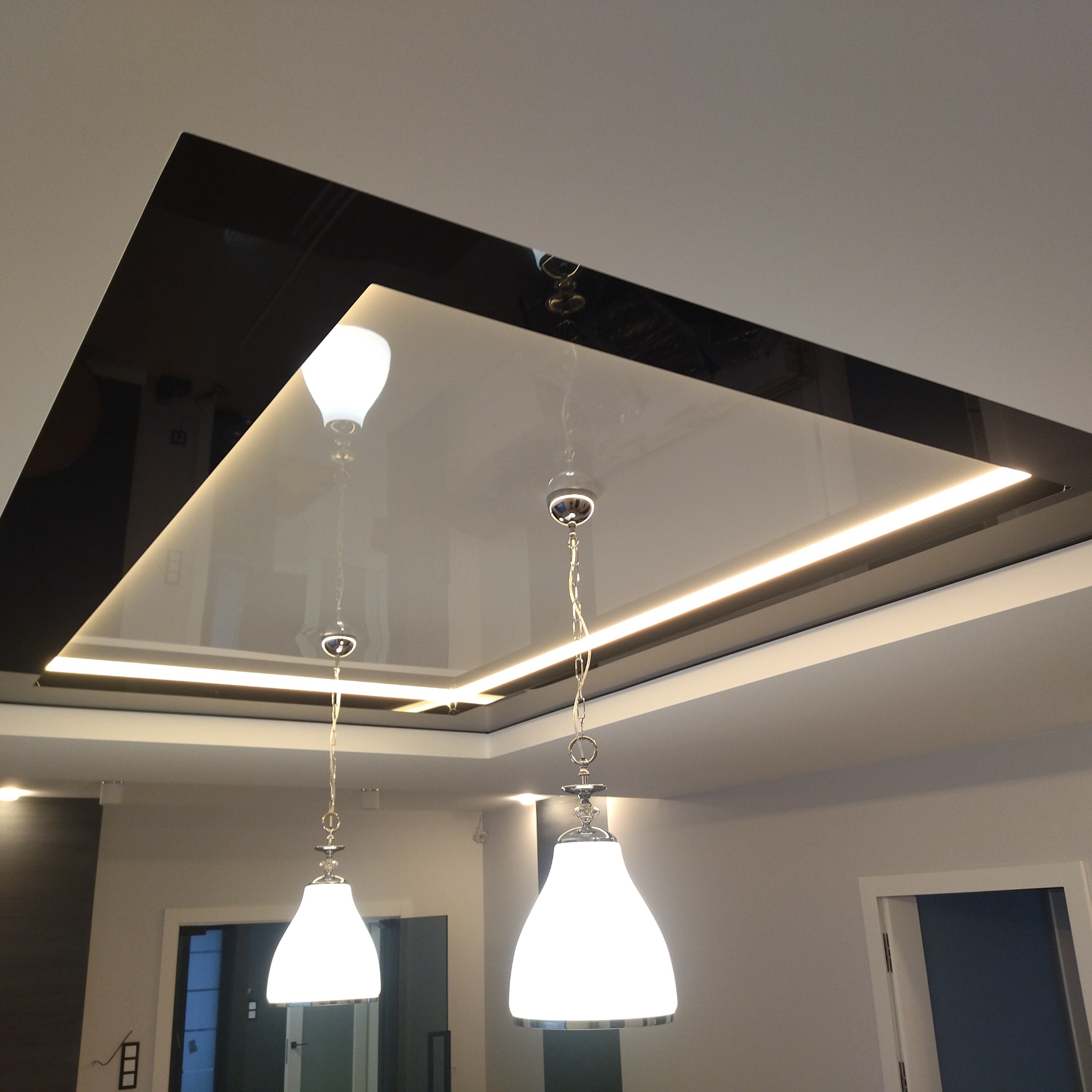 Nowoczesny sufit podwieszany z czarną obwódką i oświetleniem LED, uzupełniony o dwie wiszące lampy z białymi kloszami. Widok z dołu.