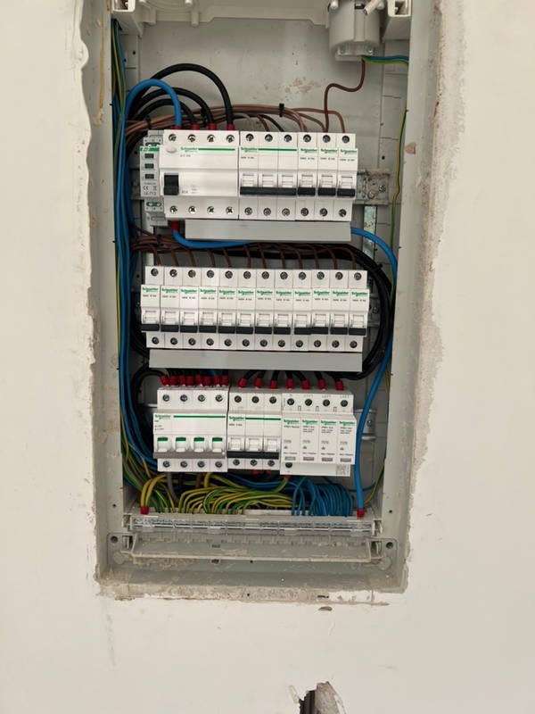 Rozdzielnia elektryczna z zamontowanymi bezpiecznikami i okablowaniem, widok z bliska na surową ścianę wokół obudowy, instalacja w trakcie prac.