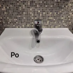 Biała umywalka po czyszczeniu, z błyszczącą armaturą i odpływem, na tle mozaiki. Widoczny fragment czerwonej rury. Napis 'Po' na umywalce.