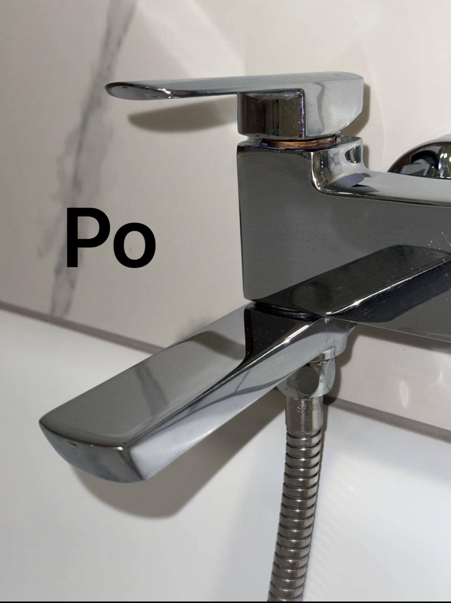 Błyszcząca, chromowana bateria umywalkowa po czyszczeniu, z widocznym napisem 'Po'. Minimalistyczne tło z białych płytek.