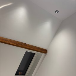 Wegner construction - Poddasze po remoncie: białe ściany, drewniana belka, okno dachowe i nowoczesne oświetlenie punktowe. Minimalistyczny design w jasnym wnętrzu.